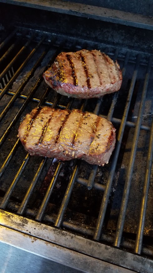 Two pork chops cooking on a shared campground gas grill during a road trip in Michigan