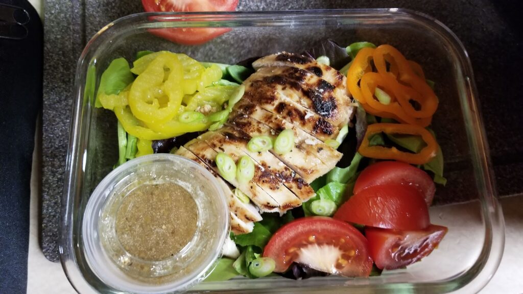 Travel lunch salad with grilled chicken, vegetables and dressing packed in a container