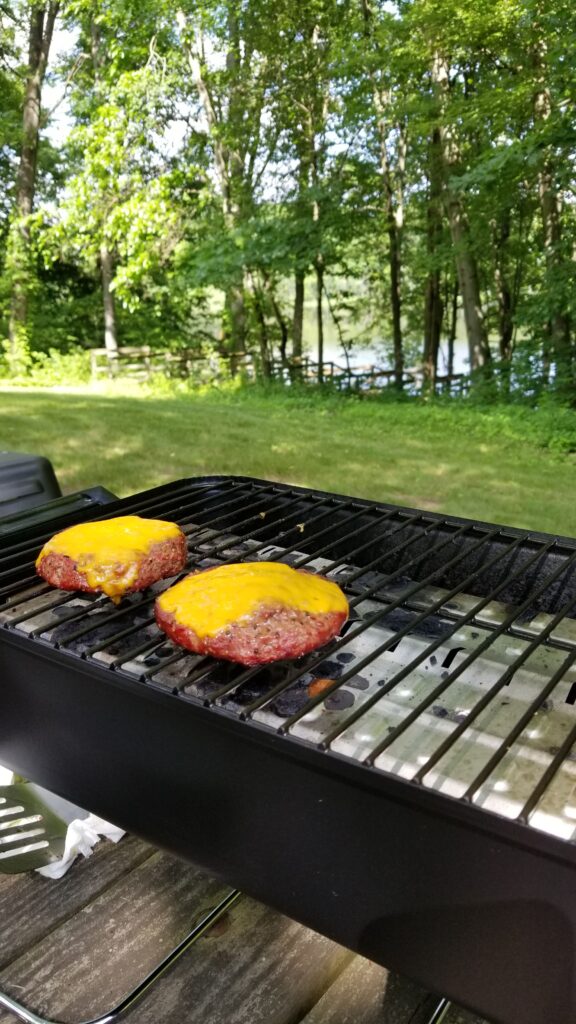 simple burgers cooking on a portable grill at a picnic table during a road trip stop