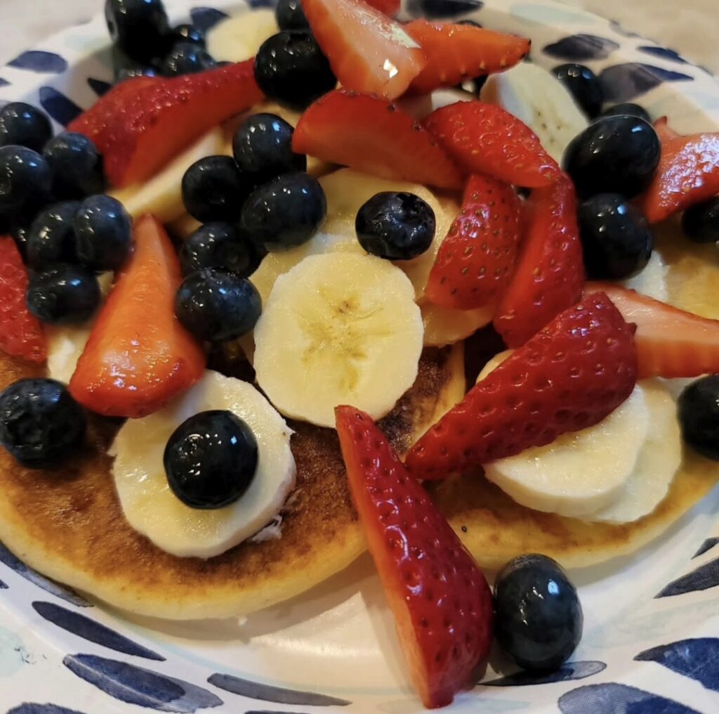 Gluten-free pancakes topped with blueberries, strawberries and banana slices.
